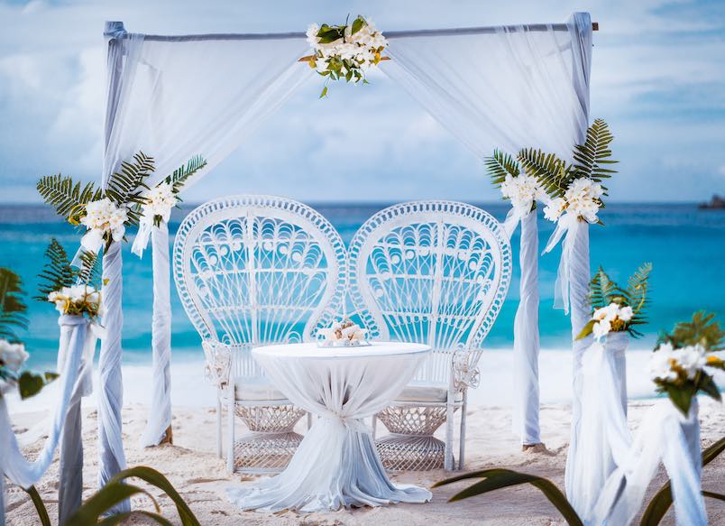 Beach wedding arch gazebo ceremonial decorated with white flowers on a tropical grand anse sand beach. Outdoor beach wedding setup. La Digue, Seychelles