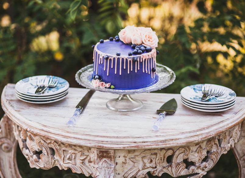 Beautiful and tasty blue wedding cake decorated with rose flowers and fresh blueberry on wooden vintage table