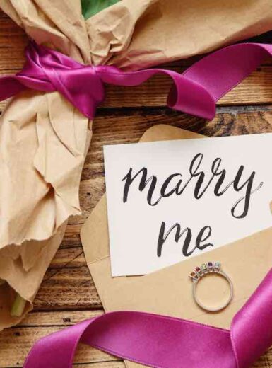 Bouquet in craft paper with a MARRY ME card and proposal ring on wooden table