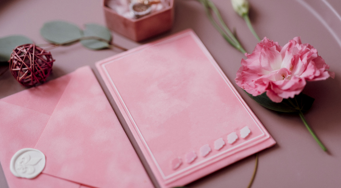 wedding invitation in a gray envelope on a table with green sprigs